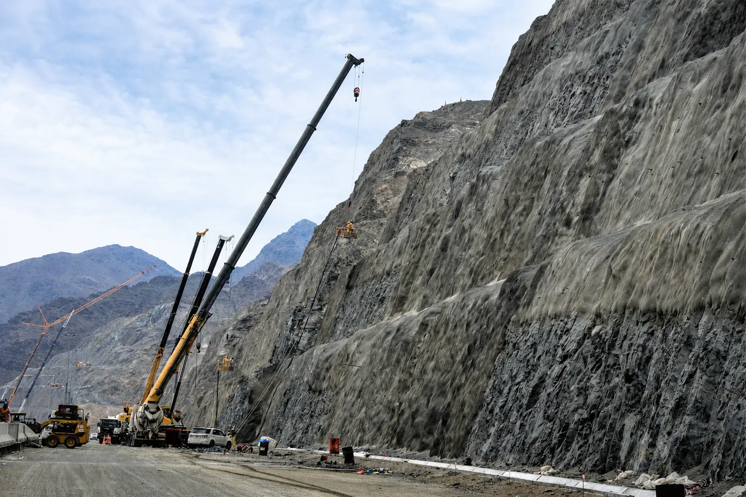 Rock slope stabilization and high-tensile mesh installation beside the live Al Watan carriageway
